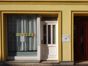 Eingang der Malkunstwerkstatt in Cottbus mit gelber Fassade, Schaufenster und Schriftzug MALKUNSTWERKSTATT